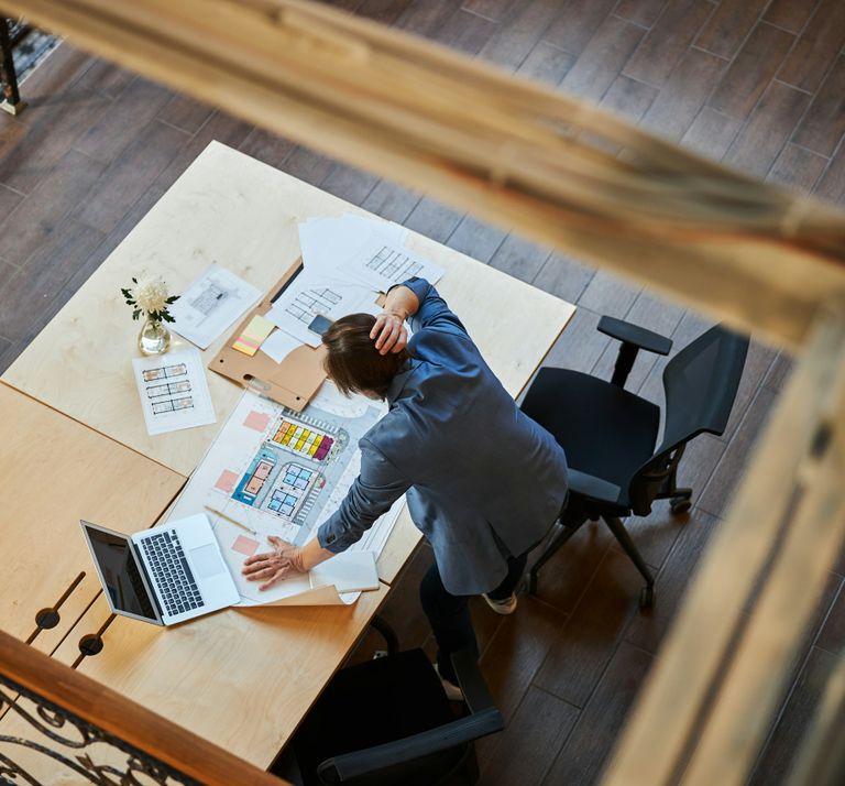 Büromitarbeiter lehnt über einem vollen Schreibtisch 