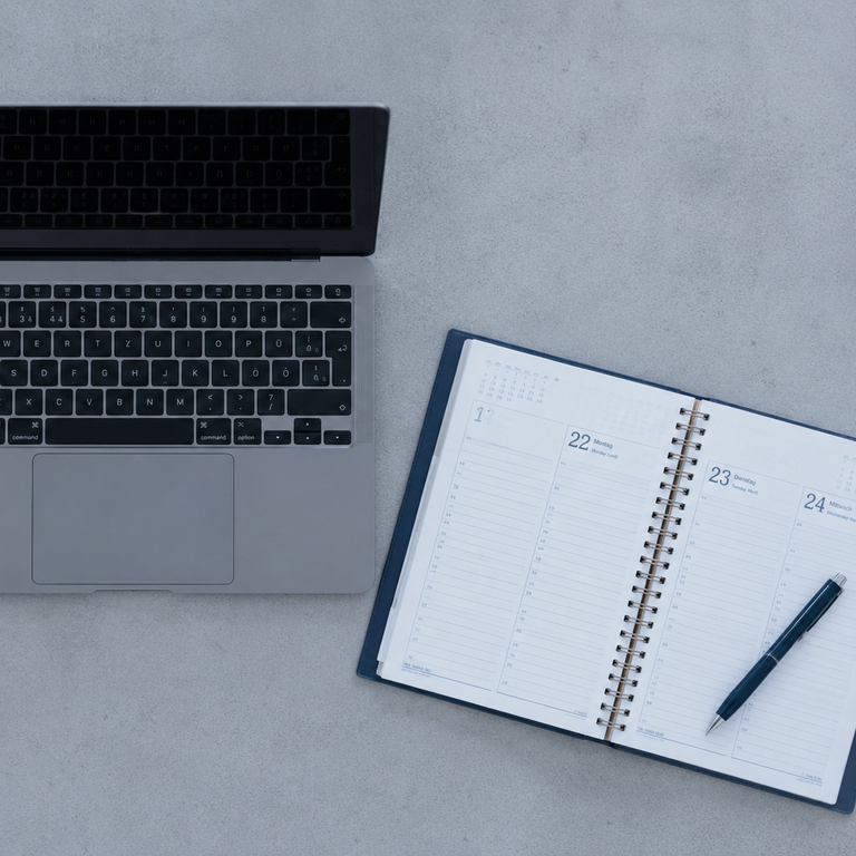 ein Laptop und ein aufgeschlagener Kalender auf einem grauen Hintergrund